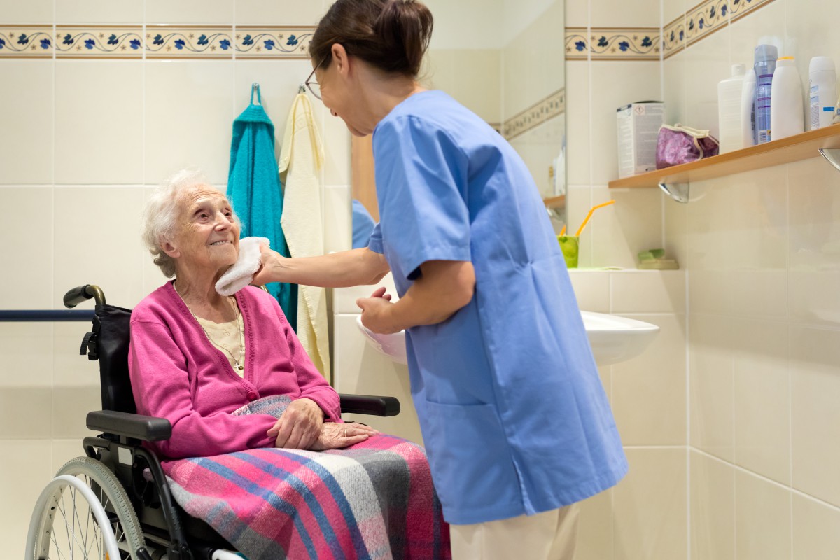 Female personal care worker washes the face of an elderly wheelchair-bound woman