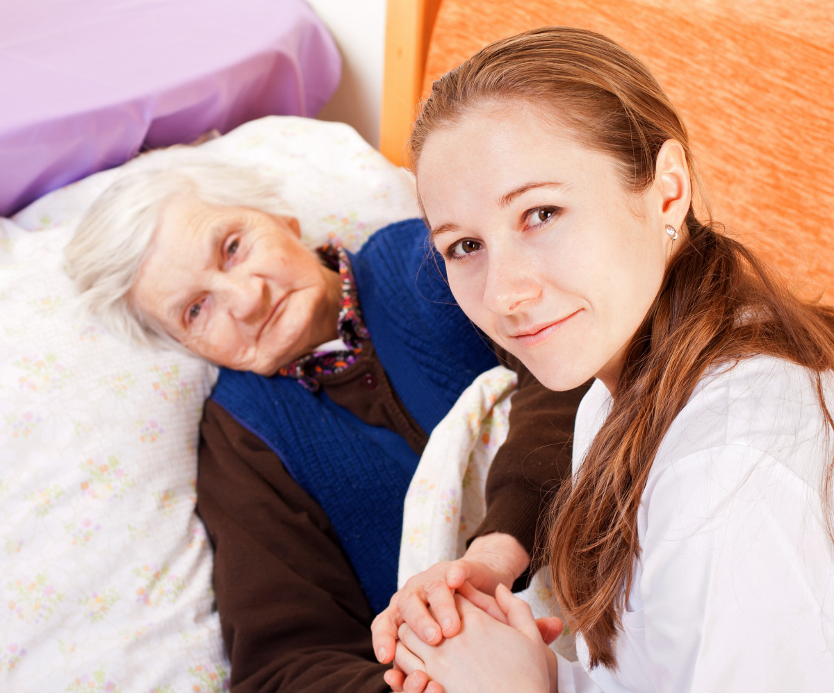 Young woman holds the hand of an elderly woman who is lying in bed.